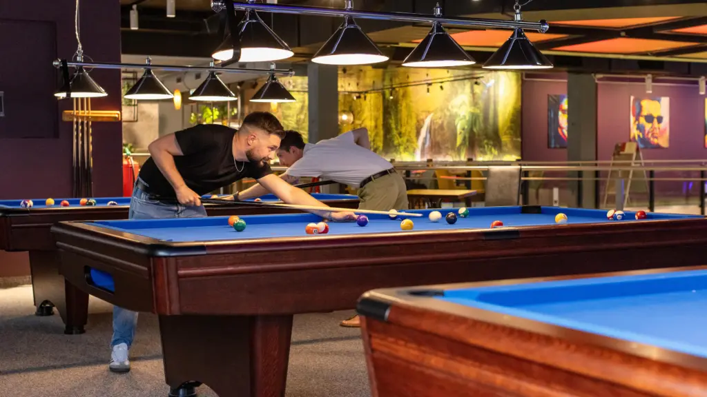Zwei Freunde zielen gleichzeitig beim Billard an mehreren Tischen im Restaurant CHILLY in St. Johann im Pongau