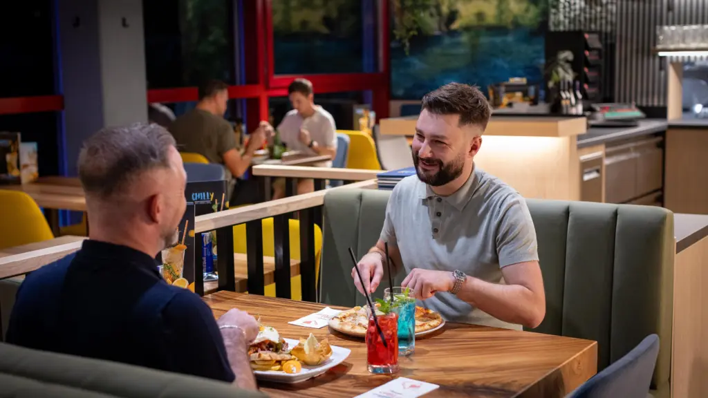 Zwei Gäste beim Essen mit Pizza und bunten Cocktails im gemütlichen Gastraum des Restaurants CHILLY in St. Johann im Pongau