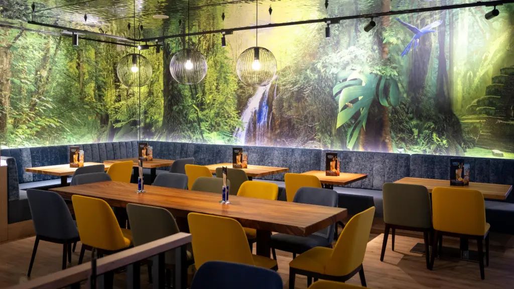 Sitzbereich mit Holztischen vor großem Dschungel-Wandbild mit Wasserfall im Restaurant CHILLY in St. Johann im Pongau