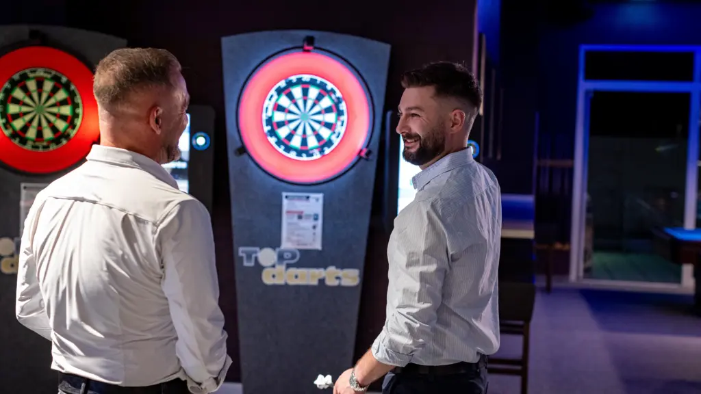 Zwei Gäste unterhalten sich lachend beim Steeldarts vor beleuchteten Dartscheiben im Restaurant CHILLY in St. Johann im Pongau