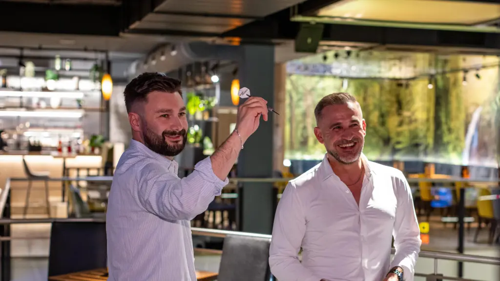 Gast zielt mit Dartpfeil beim Steeldarts-Spielen, daneben ein lachender Gast im Restaurant CHILLY in St. Johann im Pongau