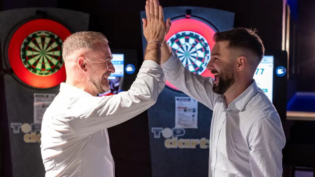 Zwei Gäste klatschen sich lachend ab beim Steeldarts-Spielen vor beleuchteten Dartscheiben im Restaurant CHILLY in St. Johann im Pongau